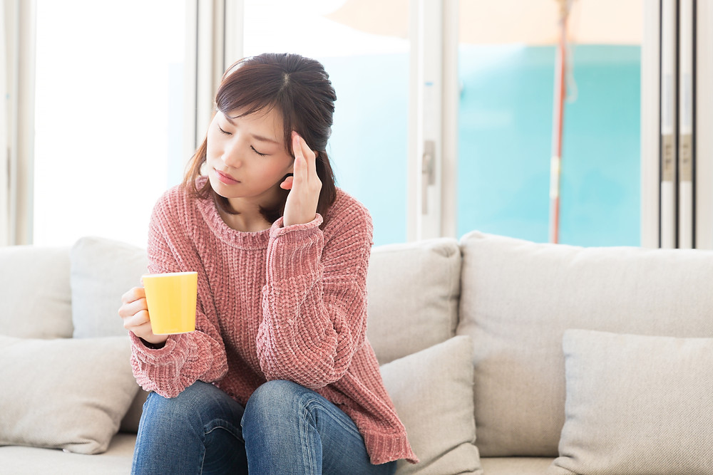 woman in pink sweater holding a mug and has a headache