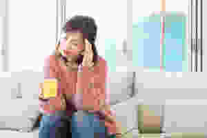 woman in pink sweater holding a mug and has a headache