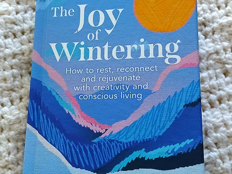 A book cover of The Joy of Wintering, with an abstract mountain range and a sun made from a ball of wool