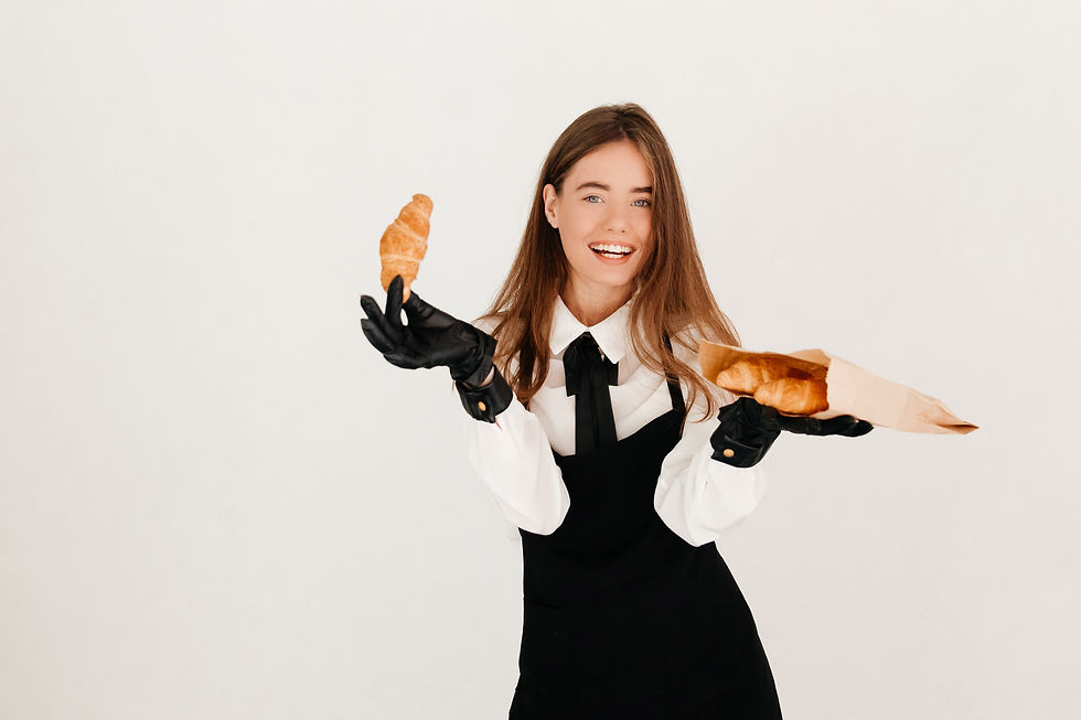 Camarera riendo con uniforme y guantes negros posando con croissants recién hechos