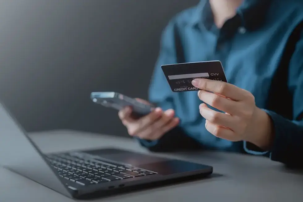 Primer plano de una persona que usa una tarjeta de crédito con una computadora portátil y un teléfono inteligente, que simboliza el pago en línea.
