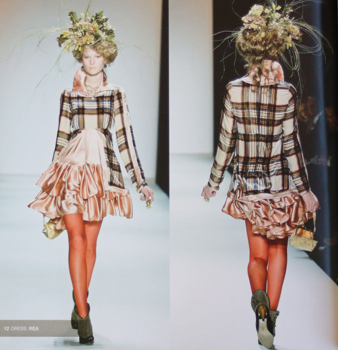 Modell auf dem Laufsteg mit aufwendiger Blütenfrisur vorne und hinten zu sehen in einem kurzen rosa Seidenkleid mit Stehkragen und langem Ärmel im Oberteil abgesetzten Karomuster und einer orangefarbenen Strumpfhose