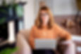 Middle aged woman using laptop and holding document in her hand while sitting at home and