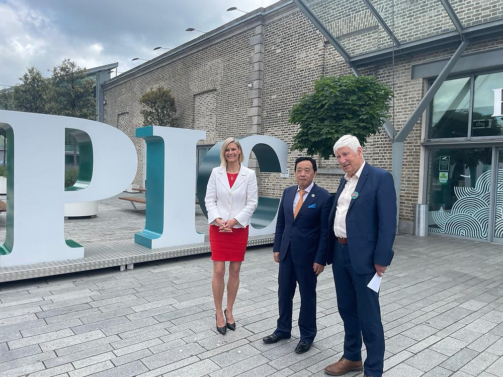 3 adults, 1 woman and 2 men, stand outside a large, old appearance building. There is 3D lettering behind them of similar size to themselves - letters are P, I, C
