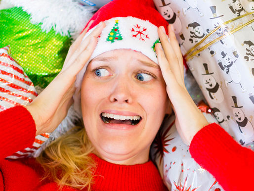 surrounded by colorful gift wrap with snowman and stripe patterns, hands on head, wide-eyed, needing peace during Christmas.
