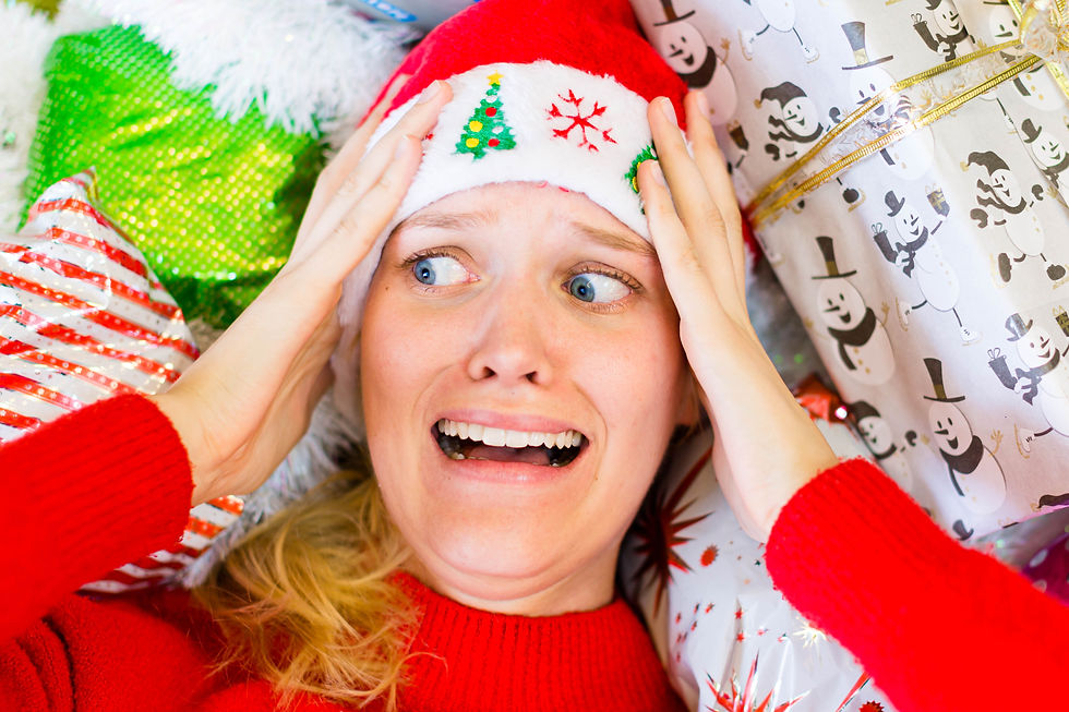 Woman in Santa hat looks stressed, surrounded by colorful gift wrap with snowman and stripe patterns, hands on head, wide-eyed, needing peace during Christmas.