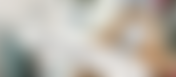 Wooden cross with floral design reads "For God so loved the world" in elegant script. Set against a vase with red flowers and decor.