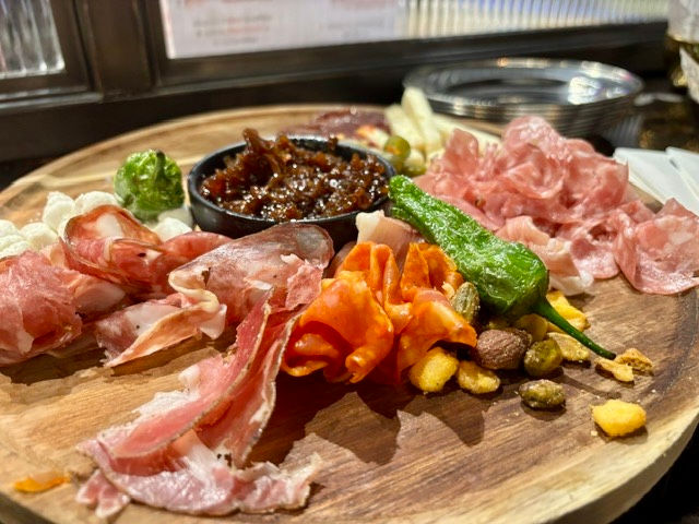 A board with slices of meat, nuts and padron peppers