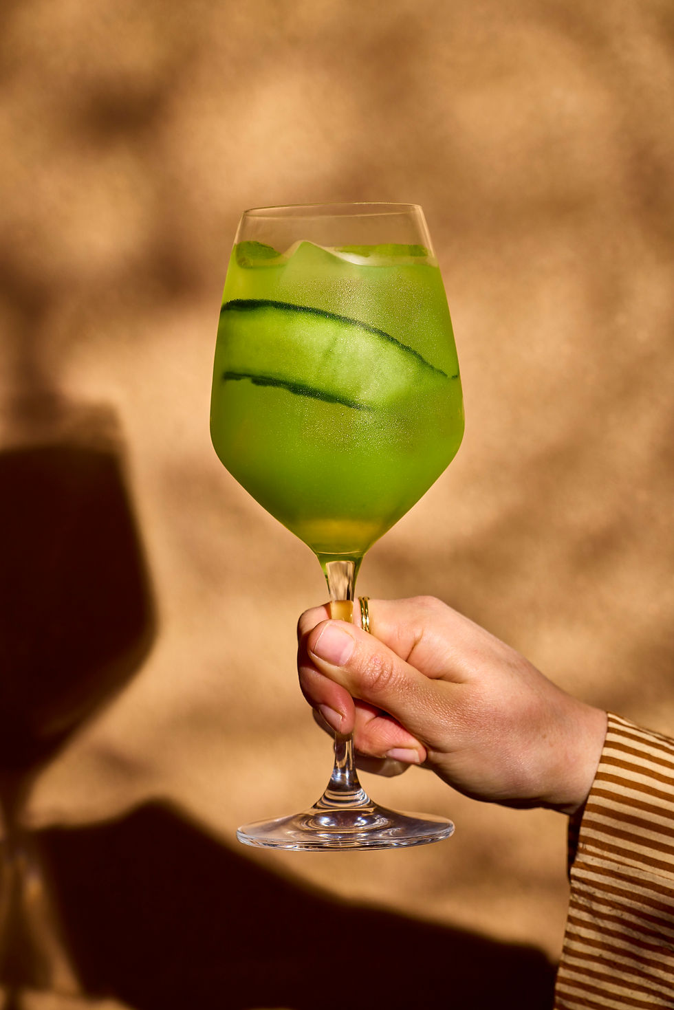 A hand holding out a Jalapeno Cucumber Sprtiz (bright green)