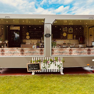 Café-Foodtruck mit zwei geöffneten Ausgabefenstern und Lichterkette, aufgebaut auf einer Wiese.