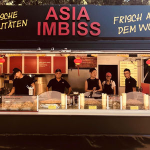 Der Foodtruck Asia Event Catering zeigt „Asia Imbiss“ auf dem Dach; Team steht an der Ausgabe, Speisekarte und Wok-Küche im Hintergrund.