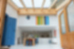 Lichtdurchfluteter Kunstraum des Atelierhaus Berg mit Glasdach, großem Arbeitstisch und farbenfrohen Kunstwerken an den Wänden.