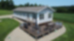 Exterior shot of a gray house with a wooden deck with furniture and Home.