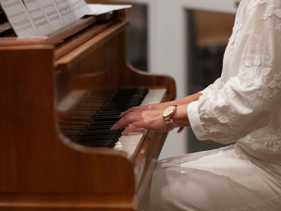 Blonde Frau mit Brille spielt gedankenverloren Klavier mit Notenblatt.