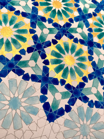 Close-up of an intricate pencil-drawn geometric pattern on white paper, highlighting the fine details of the hexagonal structure. The detailed view reveals the layered design of stars, petals, and polygons, with selective coloring in dark blue, green, light blue, and gold. The gold-painted central stars and diagonal placement of blue-filled petals enhance the sense of movement within the composition.