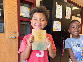 a smiling boy proudly holding up his artwork