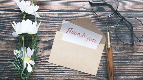 A thank you note rests on a wooden table, surrounded by flowers and glasses, creating a warm, inviting atmosphere.