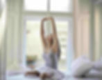 A woman performing a stretch by a window, illustrating a morning routine for an ESL lesson plan.