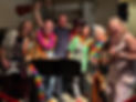 Mechanics of Music student band performing with ukuleles and guitars at a Hawaiian-themed event, smiling on stage.