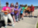 Mechanics of Music ukulele group in rainbow shirts performing outdoors at a community event.