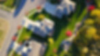 Aerial view of suburban neighborhood with houses, green lawns, vibrant red and yellow trees; a van parked in a driveway.