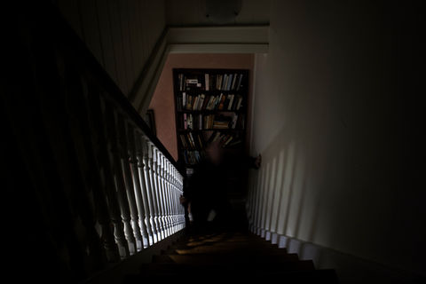 Dark staircase, light on bannister, bookshelf at bottom
