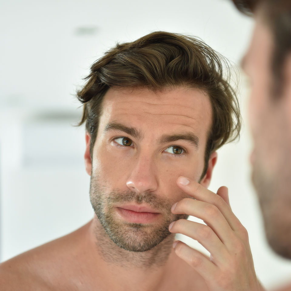 Un uomo si guarda allo specchio e si tocca la pelle.