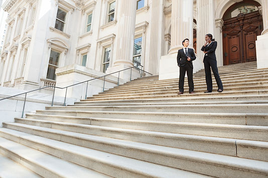 A well dressed man and woman converse on the steps of a legal or municipal building. Could