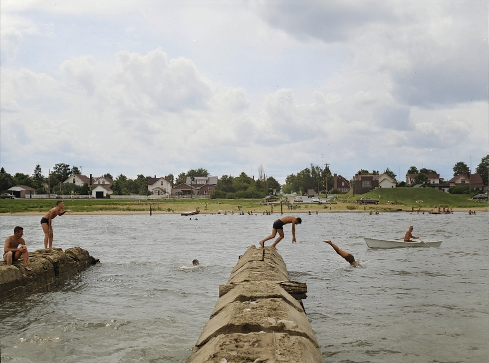 A group of older boys diving from the cement footing of the old Hoeft dock, watched closely by Lifeguard Jim Valentin from his lifeboat, 1955