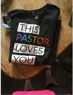 A folded t-shirt reading "this pastor loves you". The word pastor is written in rainbow letters.