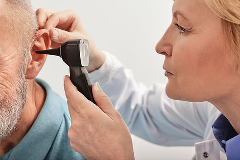 Close-up of audiologist checking elderly man ear with an otoscope during a hearing test in an audiology clinic