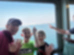 mom and two boys smiling/waving at the camera with water and an island in the background