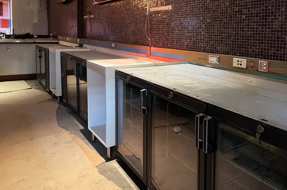 Long bar counter, glass-front refrigerators, empty interior with mosaic wall.