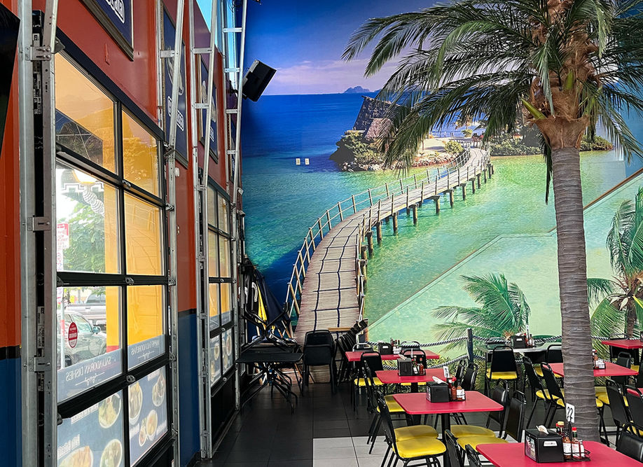 Restaurant dining area with tropical mural, palm tree, red tables, yellow chairs.