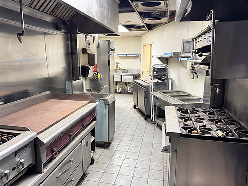 Empty commercial kitchen with stainless steel griddle, gas range, multiple sinks.