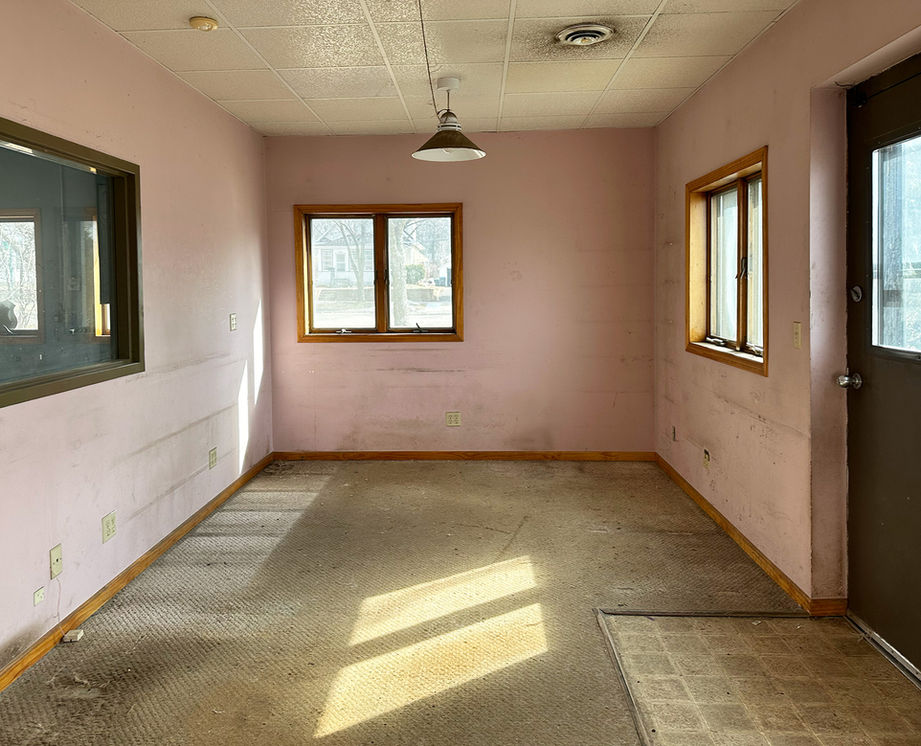 Empty room with faded pink walls, carpet, multiple windows, and door.