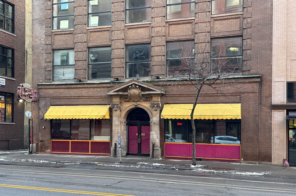 Brick building with yellow awnings and decorative entrance, pink doors.
