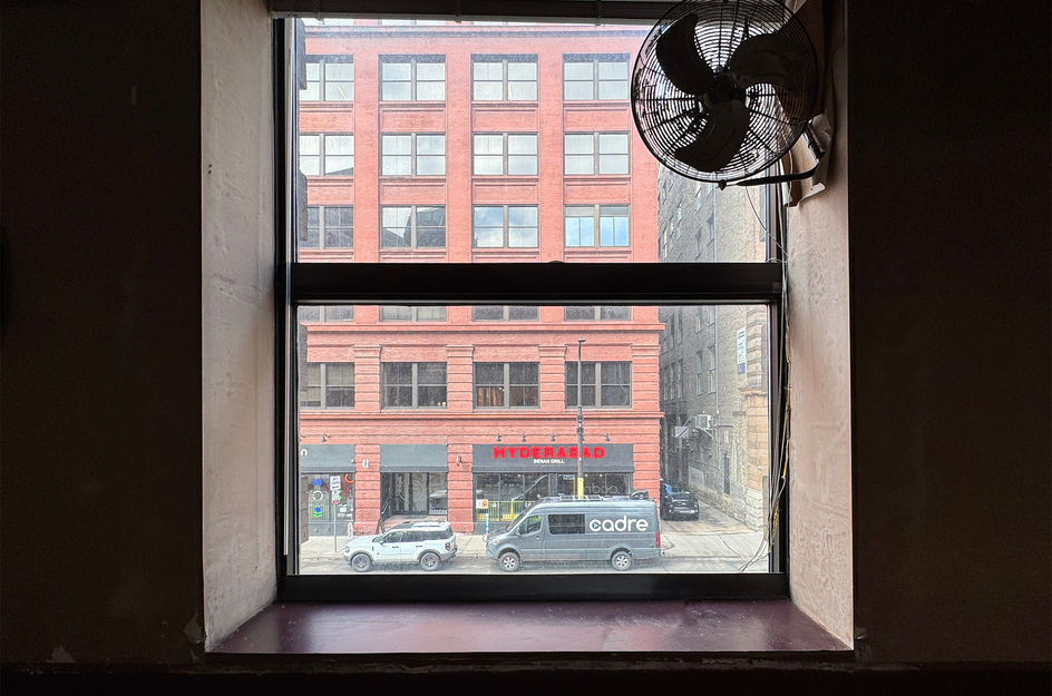 Window overlooking city street with red buildings and wall fan.