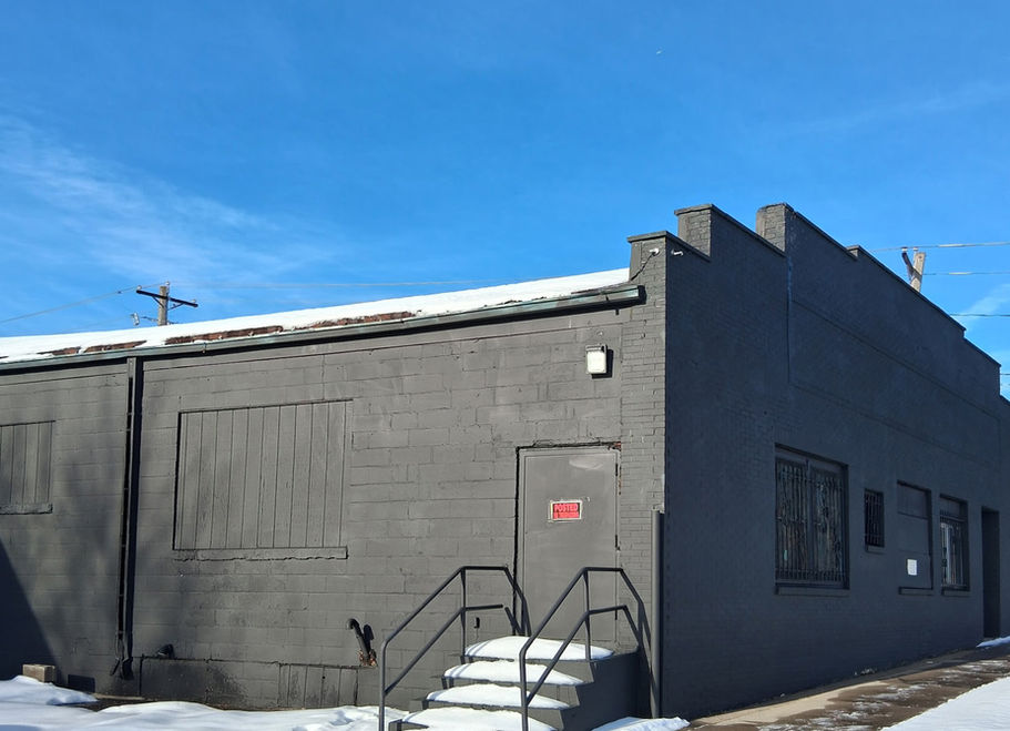Dark gray commercial building with outdoor steps, snow, and blue sky.