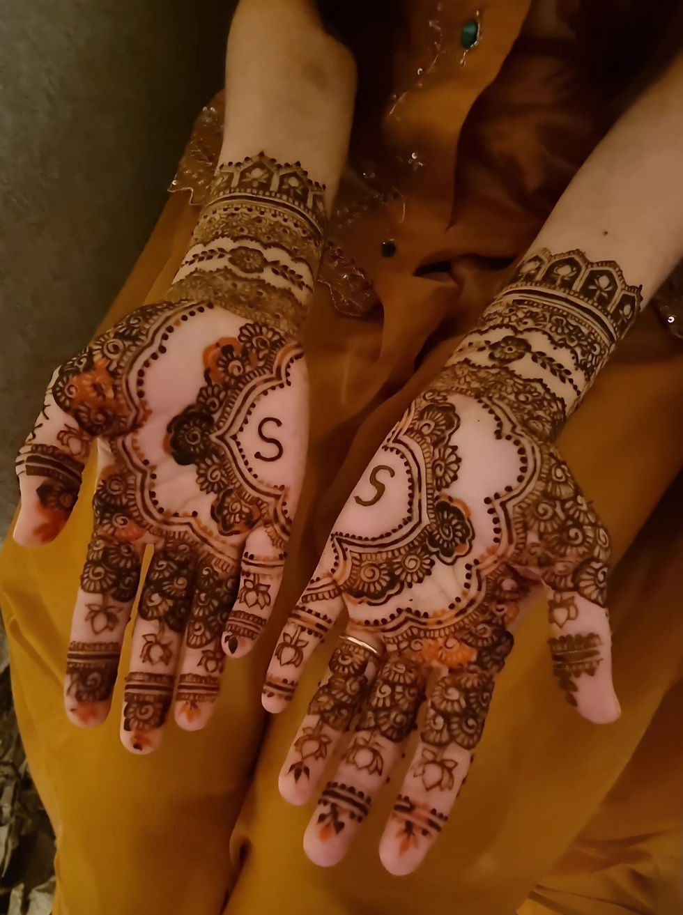 a woman 's hands are decorated with henna and the letter s is visible