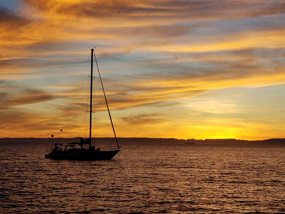 Sailboat silhouette on calm water at sunset, with vibrant orange and yellow clouds in the sky, creating a serene and peaceful mood.