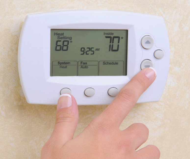 Wall-mounted white digital thermostat having its buttons pressed by hand.