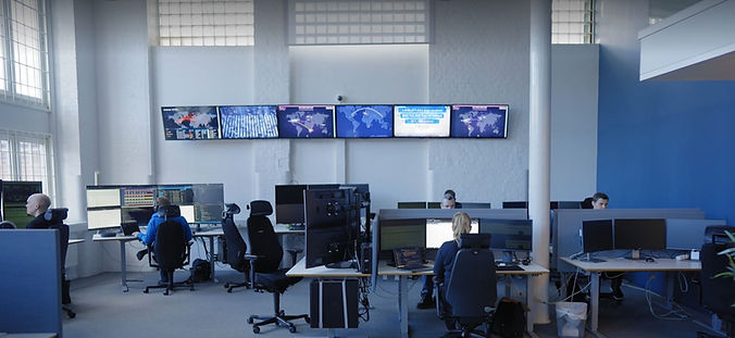 Security operations center with multiple screens and people working at computers.