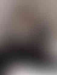 Модель у чорному вечірньому костюмі з білою квітковою аплікацією сидить, спираючись на руку, на сірому студійному фоні.