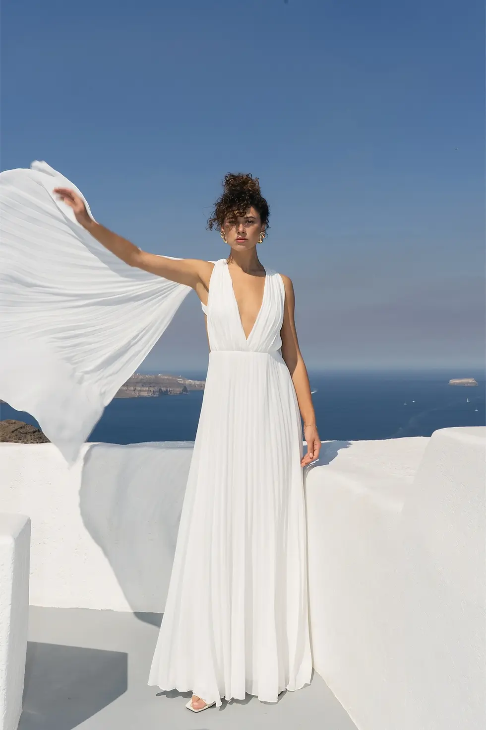 White maxi evening dress with a deep neckline, long sleeves and a pleated skirt