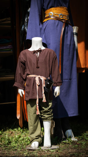 Detailgetreue Kindergewandung aus braunem und grünem Leinen auf Schaufensterpuppen präsentiert. Im Hintergrund ein elegantes blaues Leinenkleid – unsere hochwertige Auswahl für kleine und große Abenteurer.