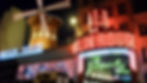 Bright neon signs of Moulin Rouge at night with a red windmill and colorful lights. Text includes "Moulin Rouge" and "Féerie Féer." Iconic cabaret show in Paris, France.