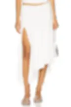 Woman in a white asymmetrical slit skirt and silver sandals, holding a silver purse, posed against a plain white studio background. What to wear in Vegas.