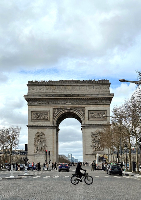 View of Arc de Triomphe with a person riding a bike across it. Paris itinerary 3 days.