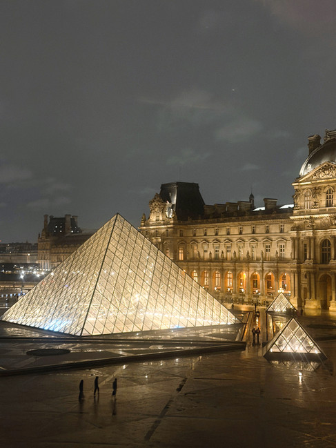 Shining lights at the Louvre Museum at night. Birds Eye view of people walking the the Lovre in the background.